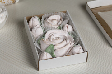 Homemade marshmallows in craft packaging. Zephyr in the form of a rose. Against the background of pine boards.