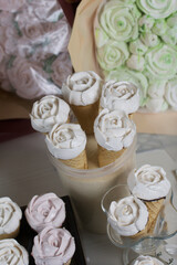 Homemade marshmallows are spread out on the table surface. Zephyr in a waffle cone. Made in the shape of a rose. Close-up shot.