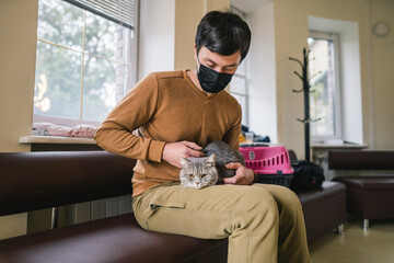 Man wearing protective mask with pet waiting in lobby for medical examination at veterinary clinic....