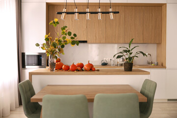 Bright modern interior, with white kitchen and pumpkins on a wooden table. 