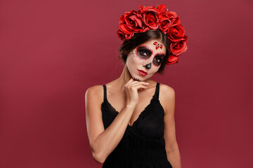 Beautiful girl in la muerta attire and skull make up looking to camera during halloween isolated on pink background.