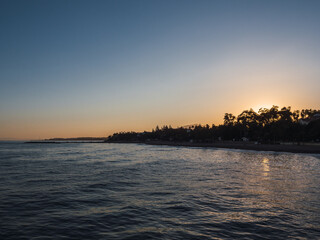 Naklejka premium Beautiful sunset by the Mediterranean sea with the silhouette of trees and palm trees in the background