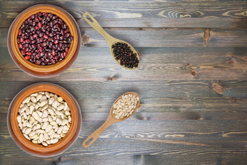 ceramic bowls with healthy grains and wooden spoons with grains on textured dark wood surface
