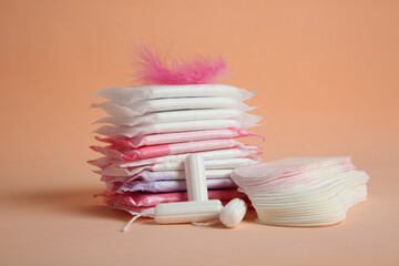 Menstrual pads with pink feather and other period products on pale orange background - obrazy, fototapety, plakaty