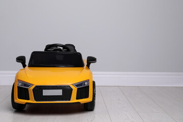 Child's electric toy car near light wall indoors. Space for text