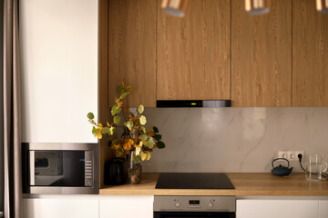 Bright interior, vase with yellow flowers stands on a wooden table in a white modern kitchen. 