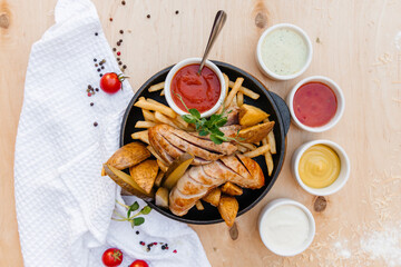 German sausages with french fries on a frying pan. With sauces. Wooden background