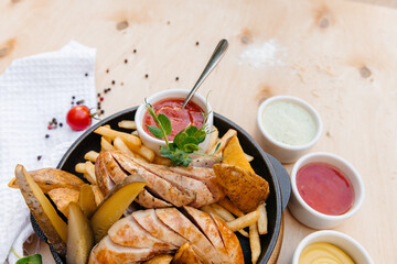 German sausages with french fries on a frying pan. With sauces. Wooden background