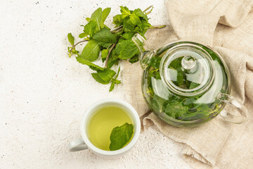 Fragrant mint tea on a light background. Glass teapot, a cup of tea, a bunch of fresh mint