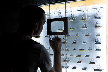 Person examines models of ships through a magnifying glass. An exhibit in the museum