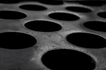 Round black holes in an old metal surface close-up. Selective focus.