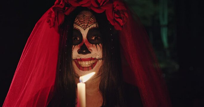 Spooky image of bride Calavera girl smiling makeup mexican skull with candle in hand