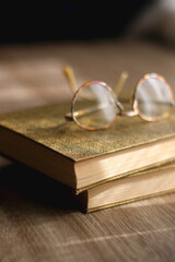 Two vintage hardback books and retro reading glasses on the table. Selective focus.