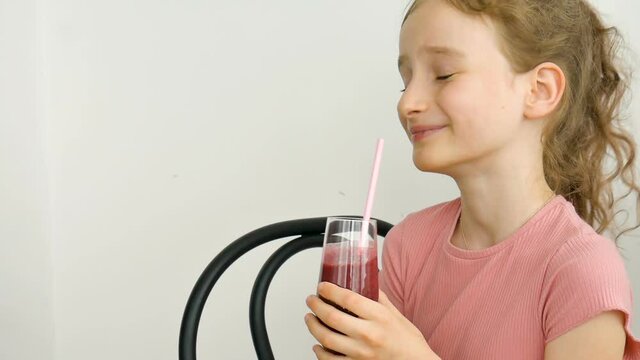 Sweet little girl drinks raspberry smoothie and smiles. Vegetarian drink. Close-up portrait of a child who enjoys a refreshing tasty raspberry juice, healthy eating