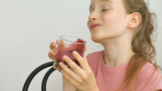 Sweet little girl drinks raspberry smoothie and smiles. Vegetarian drink. Close-up portrait of a child who enjoys a refreshing tasty raspberry juice, healthy eating