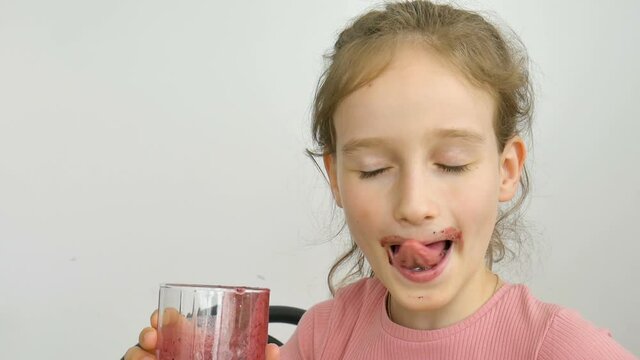 Sweet little girl drinks raspberry smoothie and smiles. Vegetarian drink. Close-up portrait of a child who enjoys a refreshing tasty raspberry juice, healthy eating