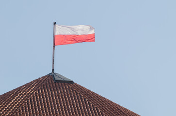 biało czerwona flaga polski zawieszona na wieży z czerwoną dachówką