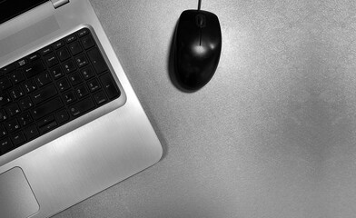 Gray laptop and a black computer mouse on a gray shiny surface. Distance learning concept in...
