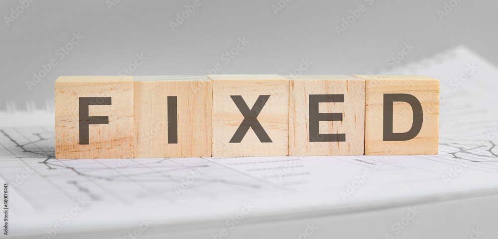 Aufkleber fixed is written on light wooden blocks. the word is located on a sheet with charts and graphs