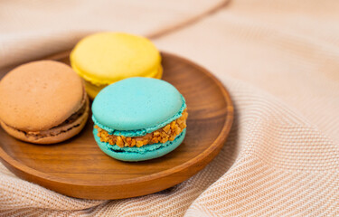 Delicious multi-colored macaroons are stacked in a wooden plate.