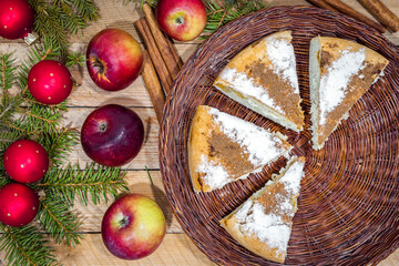 Round homemade cinnamon apple pie in a wicker plate on a wooden table with Christmas decorations around