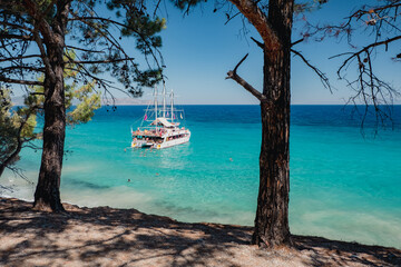 Blue sea on the Turkish coast. A boat with tourists stands near the shore. People swim in azure water. Dilek National Park, Kusadasi, Turkey