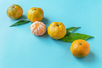 juicy ripe mandarins and bright green leaves on a blue surface close up
