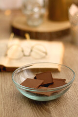 Bowl of chocolate, book, reading glasses, candles and vase with flowers on the table. Selective focus.