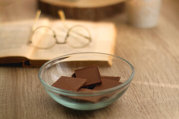 Bowl of chocolate, book, reading glasses, candles and vase with flowers on the table. Selective focus.
