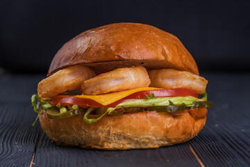 Burger with king prawns, cheese, salad, and tomato on a black wooden background.