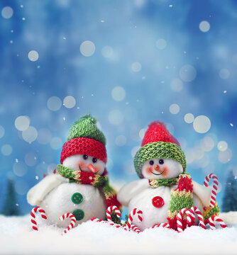 Two funny snowmen and candy cane on the snow. Christmas background.