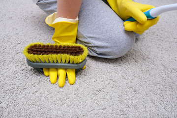 A child in yellow rubber gloves cleaning house, carpet from dust and stains with a brush