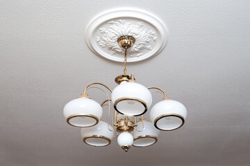 Classic candelier italian style hanging on a ceiling, lamp with 5 white lights and golden metal frame