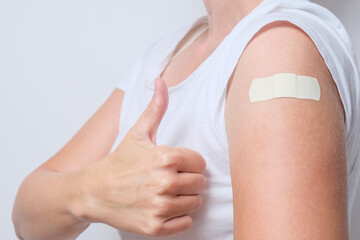 A woman showing thimb up and her arm with an adhesive bandage after injection of vaccine. Happy of getting vaccinated from corona virus, covid-19