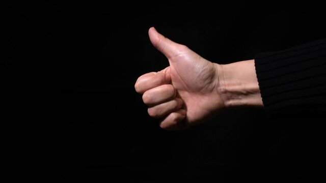 Female woman hand showing thumb up, like gesture close up in the darkness, against dark black background