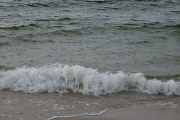 Stormy sea with light water. Small rain drops on the sea surface. White foam from the waves on the  shore.
