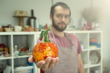 Fototapeta premium Man showing ceramic pumpkin after clay workshop lesson. Halloween eco symbol zero waste