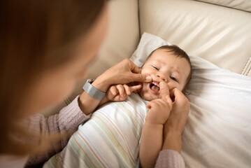 Cheerful cute baby boy lying on sofa while mother looking at his first teeth