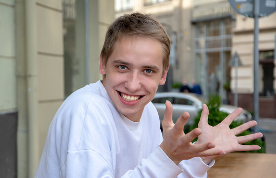 An emotional portrait of a young guy in the summer on the street with his arms outstretched.