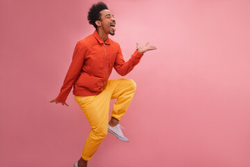 Humorous African man sticks out his tongue and raises leg with copy space. Curly brunette hair,...