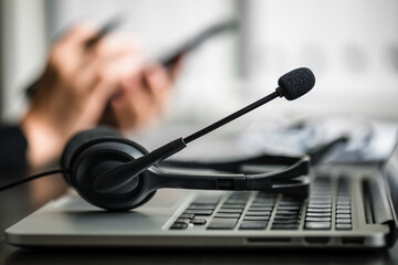 Close up view of a headset on laptop computer keyboard have women using smartphone in the background, helpdesk support, customer service, telemarketing, call center, hotline.