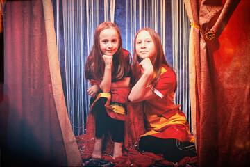 Small girls during a stylized theatrical circus photo shoot in a beautiful red location. Young...
