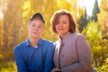 Mother and adult son in autumn park or forest in sunny day. Happy family walking outdoors