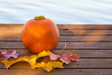 Pumpkin and autumn leaves on wooden boards with lake on the background.