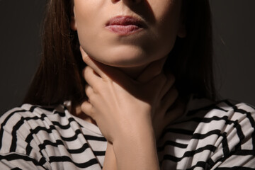 Young woman holding her throat on dark background, closeup. Concept of harassment