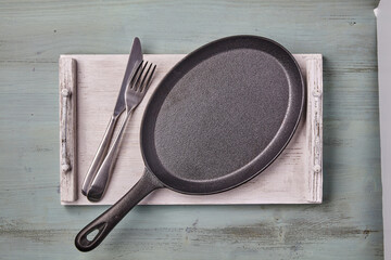 An empty oval cast iron pan on a wooden tray