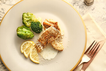 Plate with baked cod fillet, sauce and broccoli on grunge background