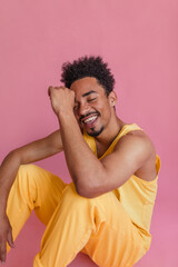 Image of happy dark-skinned man with toned body and afro hair sits on floor. He looks relaxed and confident, closing eyes while smiling in closed room. People sincere emotions lifestyle concept