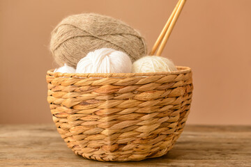 Wicker basket with knitting yarn and needles on wooden table against color background