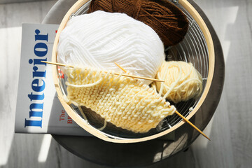 Basket with knitting yarn, needles and magazine on pouf in room, closeup